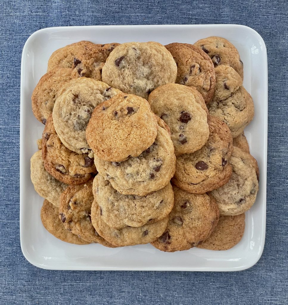 Chocolate chip cookies sit on a white plate, ready to be eaten.