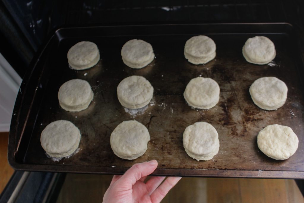 A hand is seen putting a sheet of scone dough into the oven.
