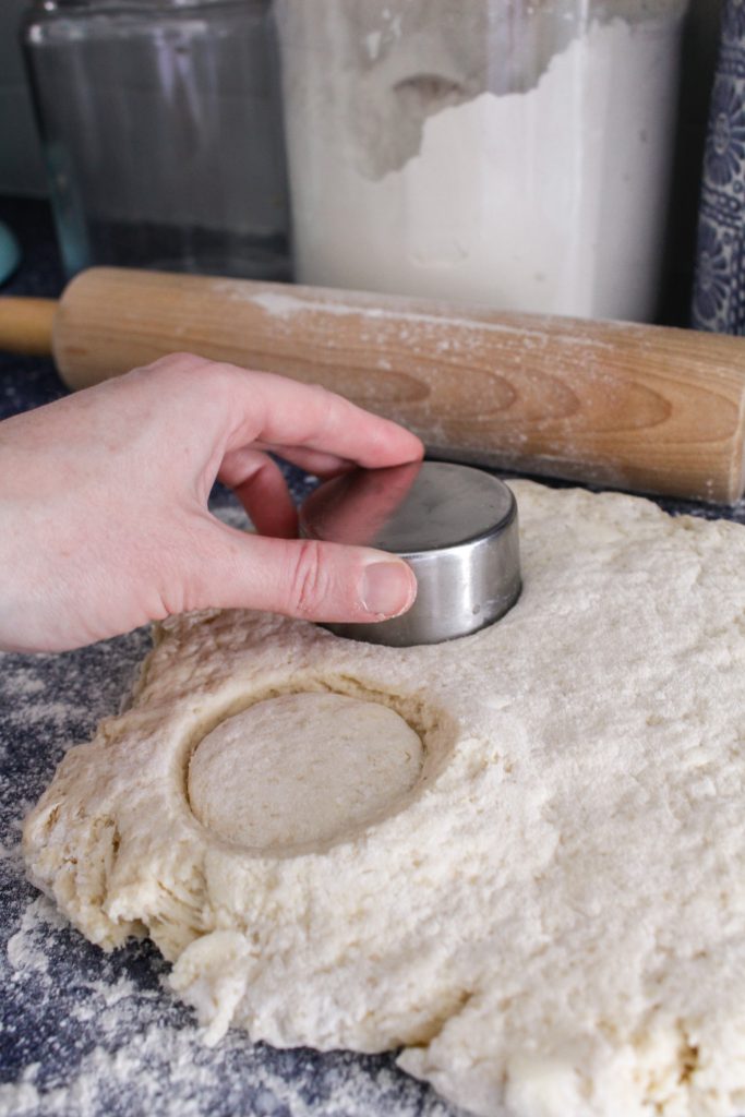 A hand using a biscuit cutter cuts circles in scone dough.