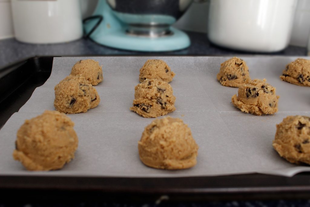 Balls of cookie dough sit on a parchment-lined cookie sheet, awaiting the oven.