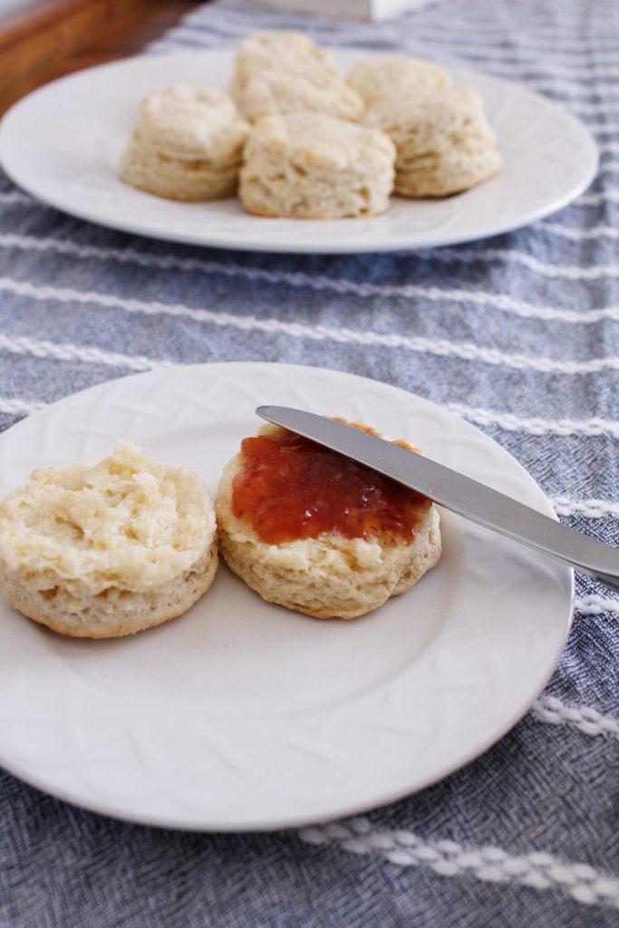 A knife is seen spreading jam on a scone.