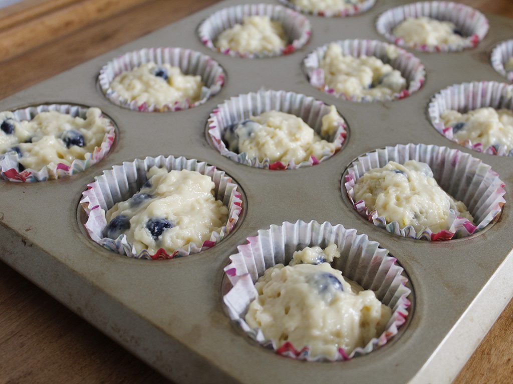 Blueberry muffin batter in lined muffin tins awaits the oven.