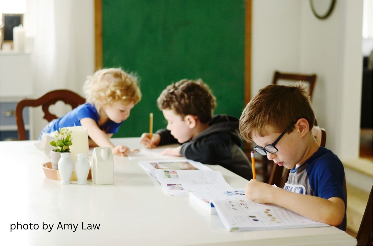 Children write in books with pencils while sitting at a table.