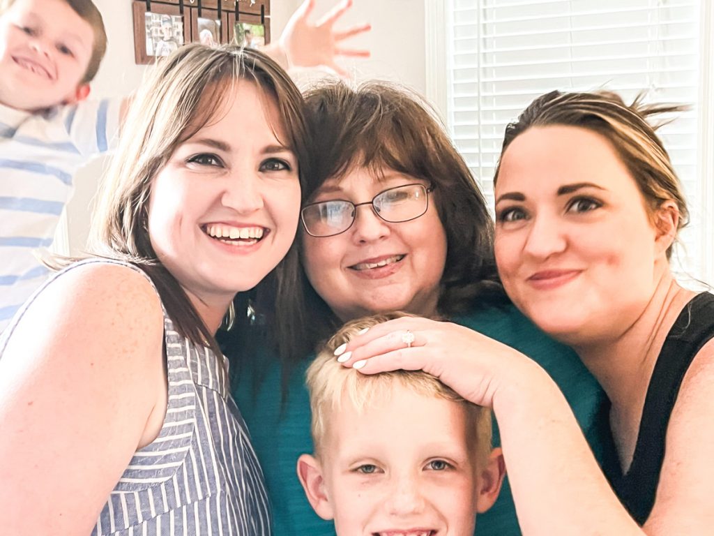 A mother, her twin daughters, and grandsone pose while another grandson pops into the background unexpectedly.