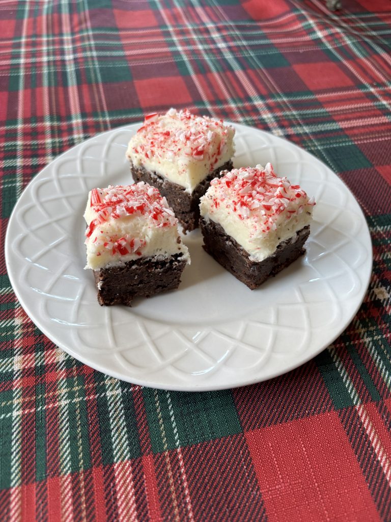 Three brownies frosted with peppermint cream frosting sit on a plate.